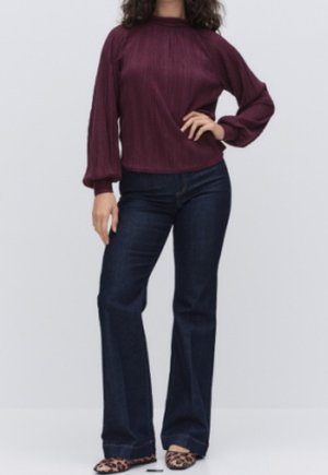 Žena oblečená v vínovém žebrovaném dlouhém rukávu, tmavě modrých zvoncových džínách a leopardích botách, stojící s jednou rukou na boku.