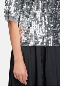 Silberner Pailletten-Shortsleeve-Top mit tailliertem Design, kombiniert mit einem schwarzen fließenden Rock. Glatte Textur und reflektierende Akzente überall.