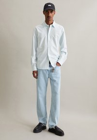 Lichtblauw gestreept overhemden, relaxed-fit licht denim jeans, zwarte platform schoenen en een zwarte pet met een wit label.