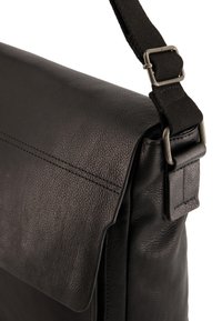 Sort læder messenger taske med flap-lukning, tekstureret overflade og justerbar kanvasrem med metalhardware detaljer.