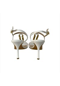 Sandali bianchi con tacco alto caratterizzati da una finitura lucida, cinturini alla caviglia e hardware con fibbia in tonalità oro, con tacco a stiletto e design aperto sul retro.