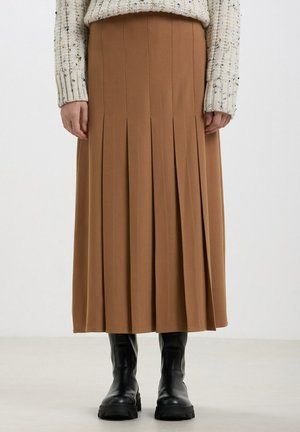 Gonna midi plissettata marrone realizzata in tessuto morbido, con cuciture verticali. Indossata con stivali neri chunky e un maglione texturizzato color crema.