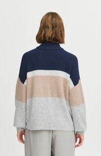 Pull en tricot bleu marine, beige et gris, doté d'un col roulé, de manches larges et de motifs en blocs de couleurs distincts. Tissu doux et texturé.