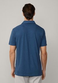 Mörkblå herrpikétröja med krage, korta ärmar och en texturerad tygkvalitet. Baksidan har en rak nederkant och minimal detaljering.