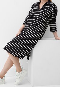 Abito a righe bianche e nere con colletto, lunghezza al ginocchio e maniche a tre quarti. Abbinato a sneakers bianche con dettagli turchesi.