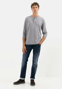 Grå langærmet henley-shirt med tre-knaps placket, kombineret med blå jeans og brune sneakers, stående på en neutral baggrund.