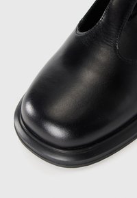 Black leather shoe with a rounded toe and smooth texture. Features a sleek design and a low, reinforced black rubber sole.