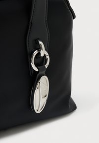 Zbliżenie na róg czarnej torby z przeszywanym skórzanym paskiem i błyszczącym srebrnym owalnym suwakiem przymocowanym metalowymi pierścieniami.