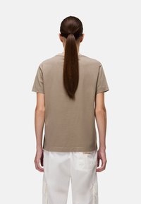 Beżowy bawełniany T-shirt z krótkimi rękawami i okrągłym dekoltem, widziany z tyłu. W połączeniu z białymi spodniami cargo, z widocznymi detalami kieszeni.