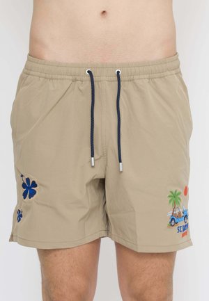 Costume da bagno beige con coulisse blu navy e disegni ricamati di fiori blu sulla gamba sinistra e una palma, un'auto e un sole sulla gamba destra.