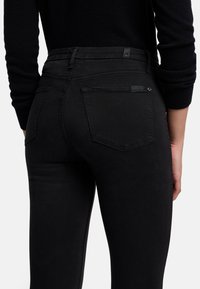 Jean skinny noir en denim, dotés de deux poches arrière, d'un design ajusté et d'une taille haute. Le tissu est lisse avec une texture minimale.