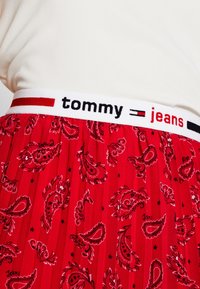 Roter, gefälteter Rock mit Paisleymuster, ausgestattet mit einem weißen elastischen Bund, auf dem "tommy" und "jeans" in schwarzer und roter Schrift steht.