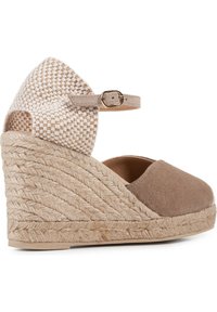 Brown suede espadrille wedge with woven beige pattern at the back, ankle strap, and braided jute sole. Angular, textured design.