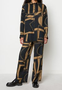 Sort og guldfarvet mønstret sæt med skjorte og bukser lavet af glat stof; har geometriske designs og en afslappet pasform med knaplukning foran.