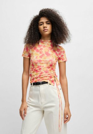 Short-sleeve, fitted top in tie-dye pattern with pink, yellow, and orange hues. Features ruched detailing on the side and a round neckline.