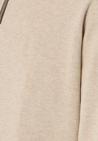 Beige Strickpullover mit einem dezenten gestickten Logo auf der Brust und einem Reißverschluss am Kragen.