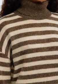 Kötött garbó pulóver széles bézs és barna csíkokkal, puha textúrával és bordázott nyakkal. Kerek forma, könnyű anyag.