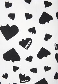 Tejido blanco con un patrón de corazones negros de diferentes tamaños, incluyendo algunos con formas recortadas, y el logo "DKNY" en texto negro.