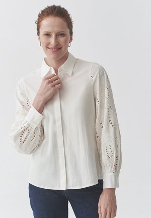 White blouse with long, embroidered, puffed sleeves featuring eyelet details. Collared shirt design with a straight hem and buttoned cuffs.