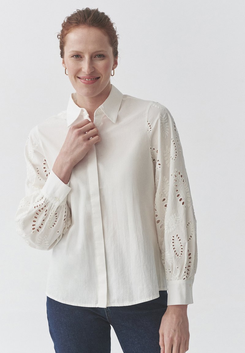 Witte blouse met lange, geborduurde, opgezette mouwen met oogjes. Kraagshirtontwerp met een rechte zoom en knoopmanchetten.