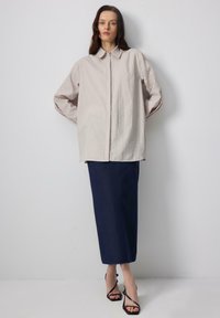 Light beige, oversized button-up shirt with a pointed collar, paired with a dark navy, ankle-length skirt and black strappy sandals.
