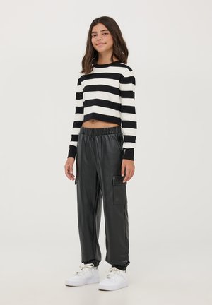 Maglione corto a righe bianche e nere, pantaloni in ecopelle nera con vita elastica e tasca laterale, abbinati a sneakers bianche.