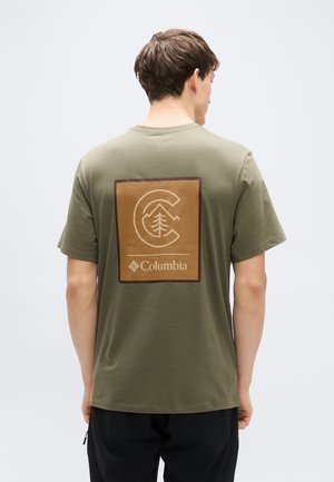 Camiseta de algodón verde oliva con un gran gráfico cuadrado marrón en la parte trasera que muestra una "C" estilizada y un diseño de árbol, además del texto "Columbia".