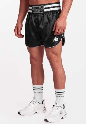 Man draagt zwarte Gorilla Wear shorts, witte Gorilla Wear sokken en witte sportschoenen, staand tegen een witte achtergrond.