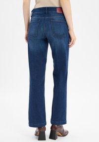 Jeans de color azul oscuro con corte recto, que cuentan con una cinturilla limpia, dos bolsillos traseros y un discreto parche con el logo cerca de la cintura.