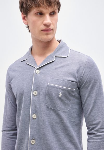 Γκρι πυτζάμα με μακριά μανίκια, γιακά με εγκοπή, λευκή διακοσμητική ρίγα, κούμπωμα με κουμπιά και τσέπη στο στήθος με μικρό λογότυπο. Μαλακό, υφασμένο ύφασμα.