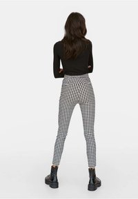 Zwart langemouwtop gecombineerd met hoogwaisted, zwart-wit geblokte leggings en chunky zwarte laarzen, gezien vanaf de achterkant.