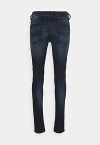 Tight jeans i mörkblå denim med en jämn textur, femfickorsdesign och en svart midja. Bakifrån syns subtila sömnadsdetaljer.