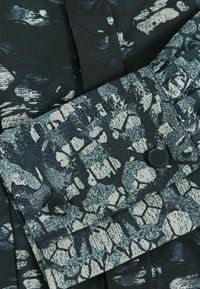 Kangas, jossa on tumma vihreä ja musta abstrakti kuvio, teksturoitu pinta, kaksi mustaa nappia ja ryppytykset.
