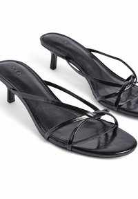 Zwarte hoge sandalen met dunne, kruisende bandjes. Gelaagd, glanzend materiaal met een vierkante neus en een bescheiden stilettohak.