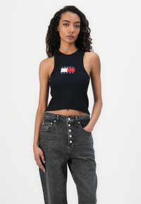 Black ribbed crop top with a round neckline featuring a multicolored Tommy Jeans logo. Paired with high-waisted gray denim jeans with button closure.