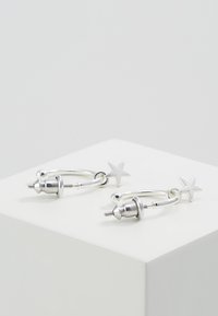 Boucles d'oreilles en argent avec de petits charms en forme d'étoile. Présentent un design arrondi et une finition métallique polie, mettant en valeur une texture lisse et un style moderne.