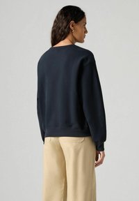 Sudadera negra de manga larga, con cuello redondo y dobladillo acanalado. Combinada con pantalones de pierna ancha en un tono beige claro. Tejido suave con un diseño minimalista.