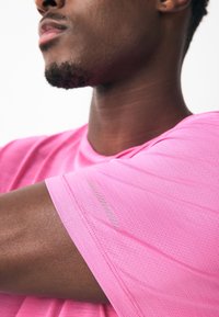 Maglietta sportiva rosa a maniche corte con tessuto traspirante e un dettaglio riflettente sulla manica sinistra.
