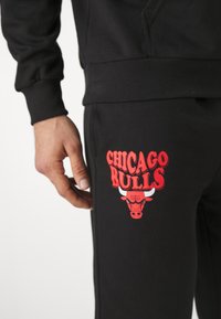 Joggers negros con gráfico rojo de "Chicago Bulls"; presenta el logo de un toro con cuernos. Hechos de una tela suave, diseño ajustado con cintura elástica.