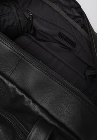 Black leather bag with a textured exterior, featuring a zipper closure and a smooth black fabric interior with a small zippered pocket.