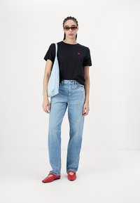 Svart t-skjorte med rødt hjerte-logo, lyseblå tote bag, lyse blå straight-leg jeans og røde flate sko. Enkelt design og klassiske farger.