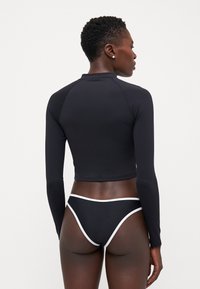 Black long-sleeve cropped top with a round neckline and a smooth texture, paired with black bikini bottoms featuring white accents.