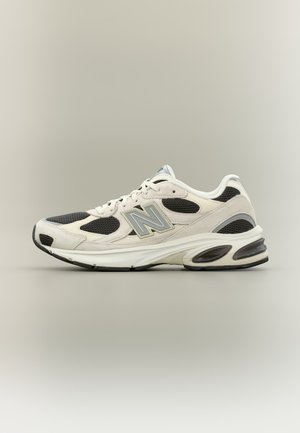 Witte en zwarte New Balance sportschoenen met meshpanelen, dikke gewatteerde zool en zijlogo "N", afgebeeld op een neutrale achtergrond.