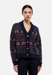 Cardigan bleu marine avec motif festif de canne en sucre d'orge et floral, doté d'un col en V, de quatre boutons marron et de poignets et ourlet côtelés. Texture douce.