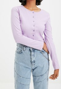 Vaaleanlila pitkähihaisten paita, jossa on pyöreä kaula-aukko, seitsemän nappia edessä ja napakat hihansuut. Yhdistetty vaaleansinisiin farkkuihin, joissa on saumat.