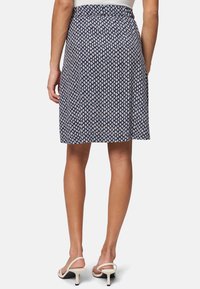 Jupe marine avec un motif en losanges blancs, taille élastique, coupe au niveau du genou, associée à des sandales à talons blancs. Tissu lisse et léger.