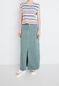 Top sans manches en coton rayé avec des lignes bleues, rouges et jaunes, associé à une jupe maxi en denim verte avec des poches latérales et une fente à l'avant.