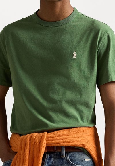Grön bomullströja med rund hals och en liten broderad logotyp. Orange stickad tröja knuten runt midjan, med struktur och ribbad design.