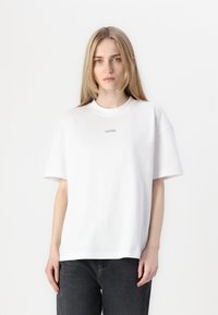 Hvit bomulls T-skjorte med avslappet passform, korte ermer og ribbestrikket rund hals. Den har en liten Calvin Klein-logo på brystet.