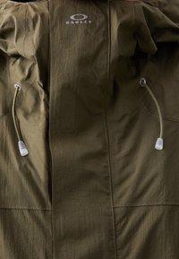 Veste d'extérieur vert olive avec cordons à l'avant et logo Oakley imprimé en blanc près de la zone du col.